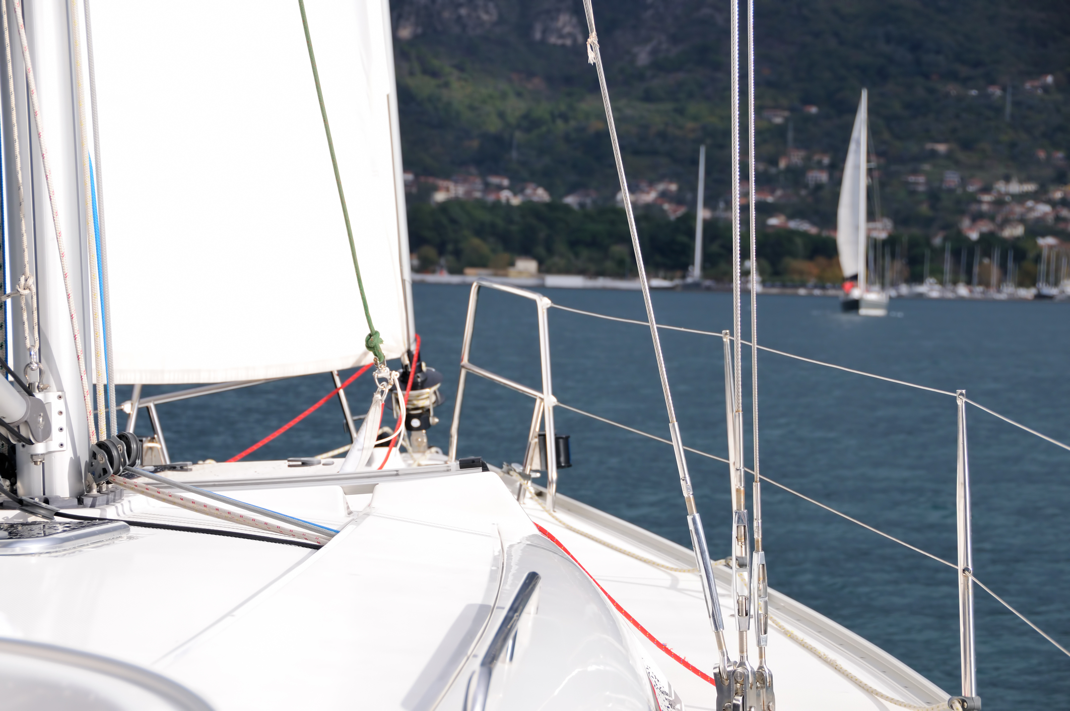 Cruising yacht under full sail on a close reach along a low coastline, seen from the cockpit with the helm's hand on the wheel and a channel buoy ahead