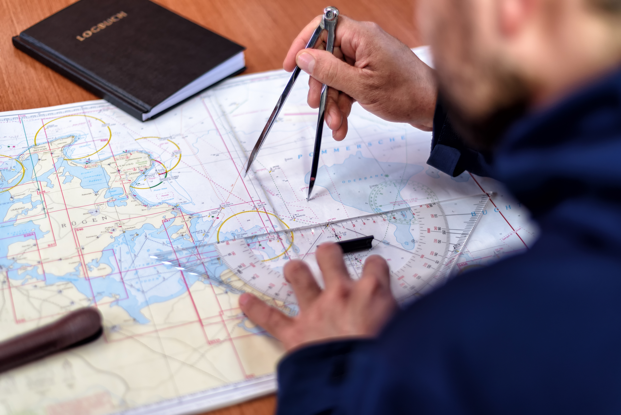 RYA training chart on a table at home with a Portland plotter, dividers, pencil and the RYA Training Almanac open at a tide table